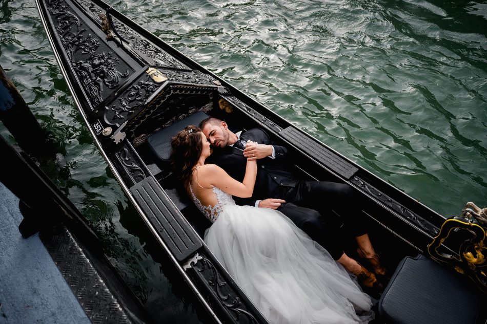 Bride and groom laying down cuddling in a gondola in Venice